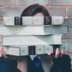 person holding pile of books near face